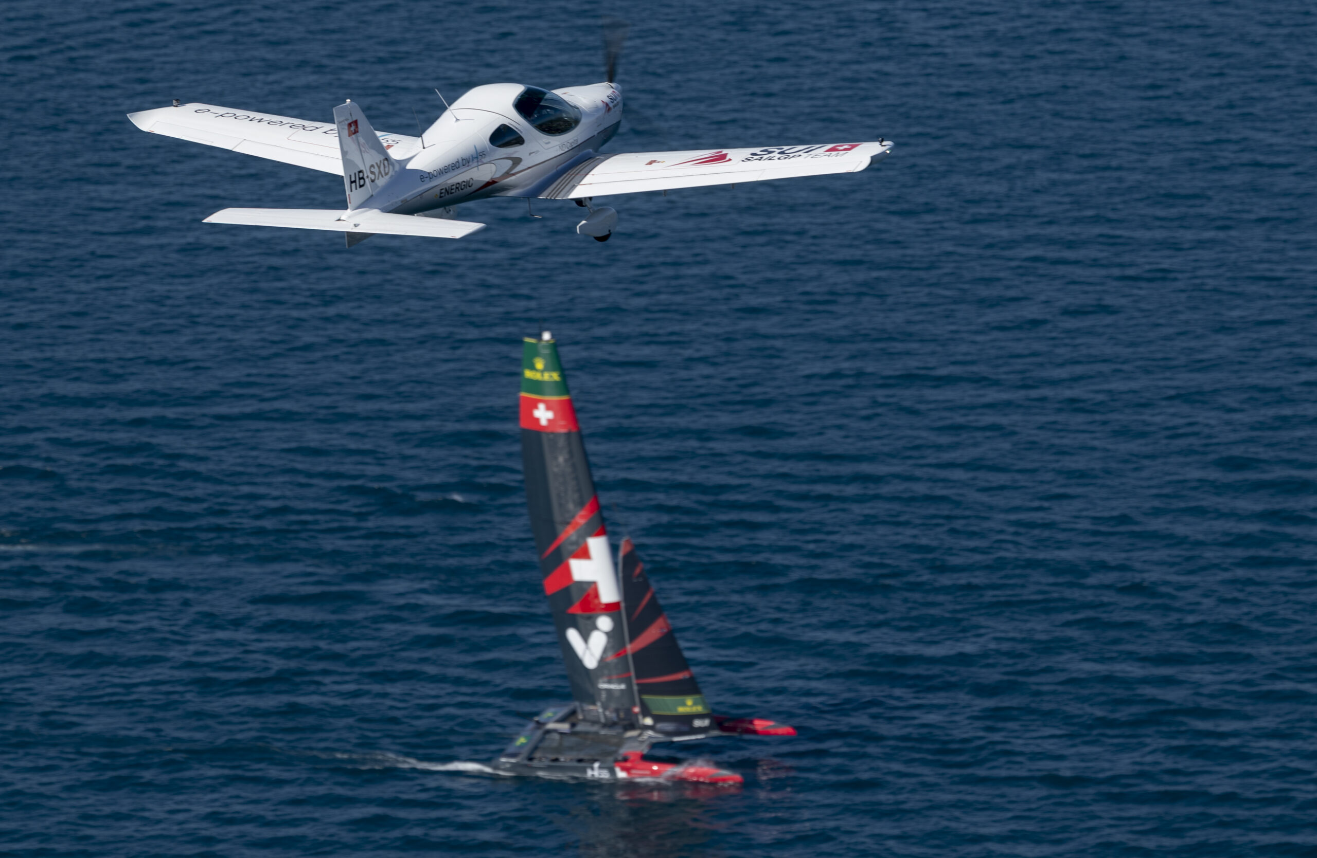 Switzerland SailGP Team branded aeroplane flying overhead as the Switzerland SailGP Team helmed by Sebastien Schneiter sail below during a practice session ahead of the Rolex Switzerland Sail Grand Prix held in Geneva, Switzerland Friday 19 September 2025. Rolex SailGP Championship Event 10 2025 Season. Photo: Samo Vidic for SailGP. Handout image supplied by SailGP